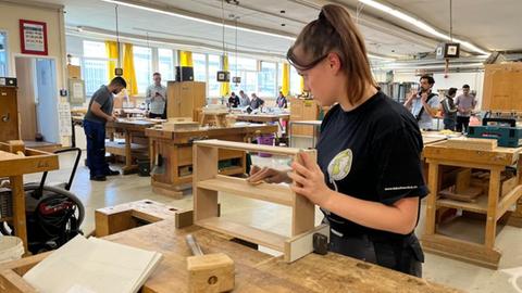 Eine junge Frau arbeitet an einer Werkbank mit Holz.