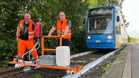 An der Endstation "Wolfsanger" lackieren zwei KVG-Mitarbeiter in orangener Sicherheitskleidung Schienen gegen die Hitze weiß, im Hintergrund eine Straßenbahn der Linie 7.