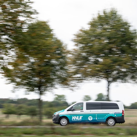 Ein elektrischer Kleinbus des Betreibers Knut fährt im Frankfurter Norden auf einer Straße mit Bäumen.