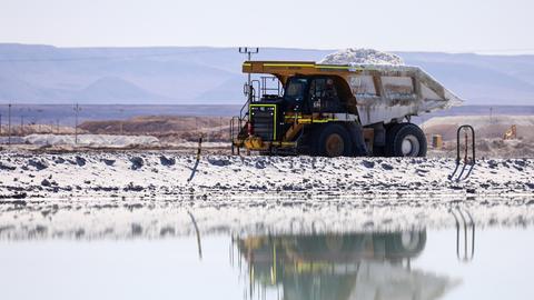 Ein Lastwagen mit offener Ladefläche, beladen mit Lithium, fährt über eine Lithium-Mine, der Boden schimmert ganz weiß vom Rohstoff