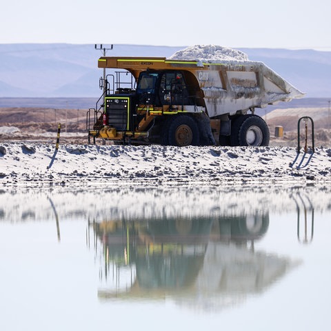 Ein Lastwagen mit offener Ladefläche, beladen mit Lithium, fährt über eine Lithium-Mine, der Boden schimmert ganz weiß vom Rohstoff