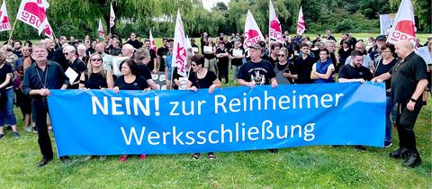 Eine Menschenmenge hält ein blaues Banner auf welchem in weißer Schrift "NEIN! zur Rheinheimer Werksschließung" steht