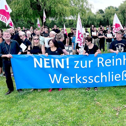 Eine Menschenmenge hält ein blaues Banner auf welchem in weißer Schrift "NEIN! zur Rheinheimer Werksschließung" steht