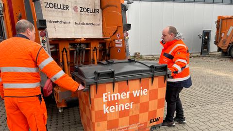 Zwei Wiesbadener Stadtreiniger heben eine Tonne an.