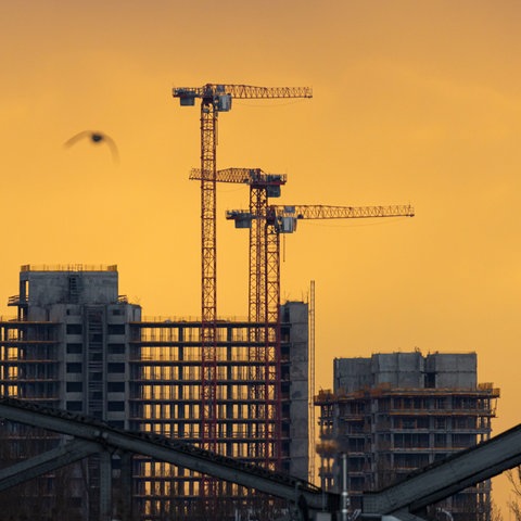 Im Gegenlicht der aufgehenden Sonne zeichnen sich beim Blick von der Flößerbücke in Frankfurt am Main die Hochhäuser und Baukräne der Großbaustelle am Kaiserleikreisel in Offenbach am Main ab.