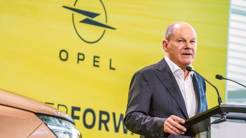 Bundeskanzler Olaf Scholz (SPD) am Rednerpult vor Opel-Logo