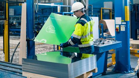 Mitarbeiter in Produktionhalle hält Metallplatte hoch mit grüner Verpackung und der Aufschrift Circle Green