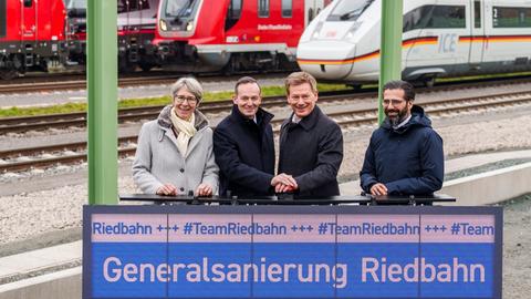 Vier Menschen zwischen Bahngleisen und vor Zügen hinter einem Display mit der Aufschrift "Generalsanierung Riedbahn", darunter mittig Verkehrsminister Volker Wissing (2.v.l.) und Bahn-Chef Richard Lutz (3.v.l.)