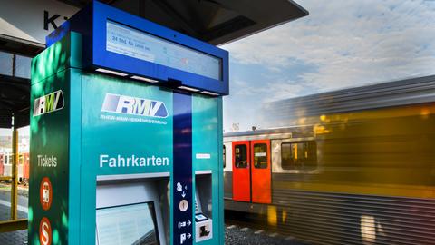 Ein Fahrkartenautomat des RMV in Friedrichsdorf. Im Hintergrund fährt eine Regionalbahn vorbei.