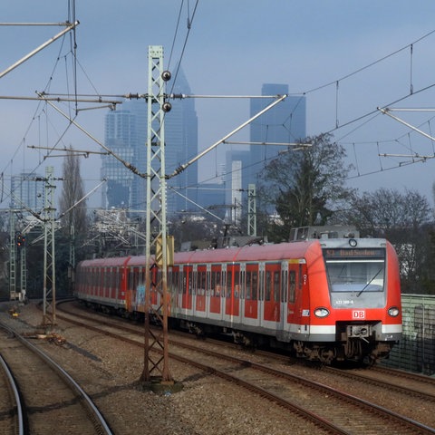 Eine rote S-Bahn fährt auf einem Gleis vor der Frankfurter Skyline