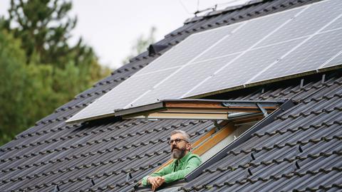 Ein Mann schaut aus dem Dachfenster, auf dem Dach sind Solarzellen installiert.