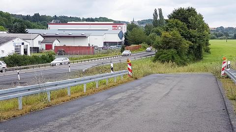 Foto einer Straße, die sich zu einem Acker neigt und abrupt endet. Daneben eine befahrene Straße.