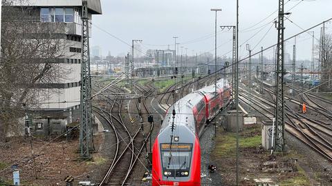 Aus der Vogelperspektive ein riesiges Areal mit sehr vielen Bahngleisn. Auf einem fährt eine Regionalbahn. Links im Bild ein Gebäude mit der Aufschrift "Frankfurt Höchst". 