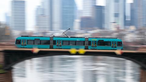 Eine türkise Straßenbahn fährt über eine Brücke, im Hintergrund ist die Skyline zu sehen.