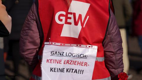 Eine Kundgebungsteilnehmerin trägt bei einem Streik die Aussage „Ganz logisch: Keine Erzieher- Keine Kita!!!“ auf dem Rücken über einer Weste der Gewerkschaft GEW.