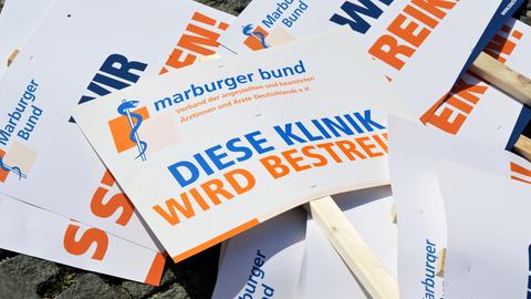 Einige Streiktafeln und Flyer mit den Aufschriften "Diese Klinik wird bestreikt" und "Marburger Bund" in orangfarbener und blauer Schrift liegen übereinander.