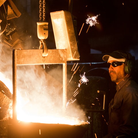 Gießerei eines Autozuliefer-Betriebs - ein Mann in Schutzkleidung neben Kessel mit flüssigem Stahl