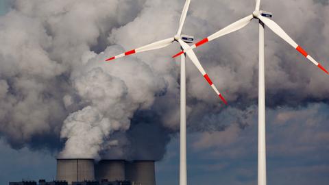 Windräder drehen sich vor den Kühltürmen eines Braunkohlekraftwerks.