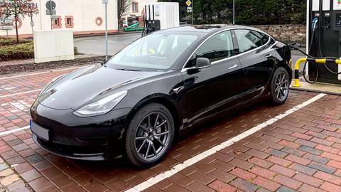 Ein schwarzes Auto - Tesla - steht an einer E-Ladesäule auf einem Parkplatz.