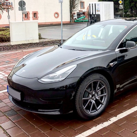 Ein schwarzes Auto - Tesla - steht an einer E-Ladesäule auf einem Parkplatz.