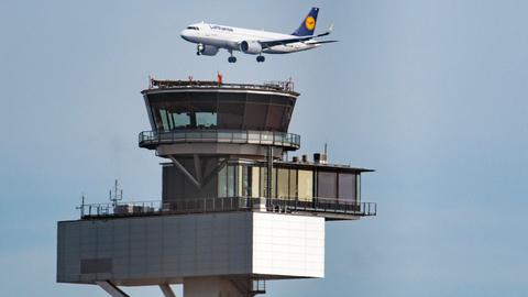 Ein Flugzeug setzt über dem Tower an einem Flughafen zur Landung an.