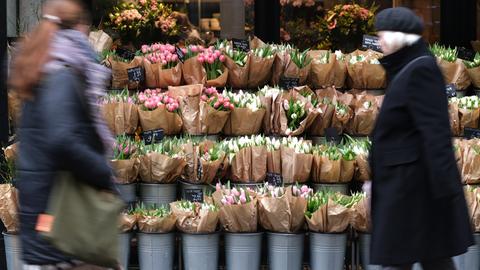 Zwei Frauen laufen an einem Blumenladen vorbei, der Tulpensträuße anbietet.