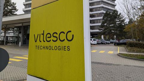 Gelbes Schild mit Aufschrift "Vitesco" vor grauem Gebäude