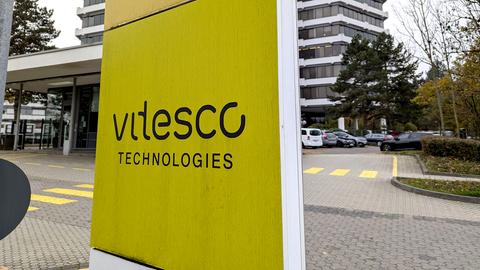 Gelbes Schild mit Aufschrift "Vitesco" vor grauem Gebäude