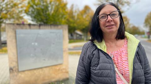 Eine Frau steht bei VW in Baunatal vor einer Erinnerungstafel. Sie hat lange, dunkle Haare und eine Brille.