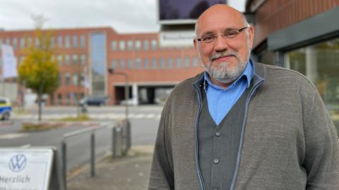 Ein Mann steht vor dem VW-Werk in Baunatal. Er trägt einen grauen Bart und eine Brille. Er hat eine Glatze.