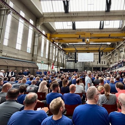 Mitarbeiter von VW sitzen in einem Saal. 