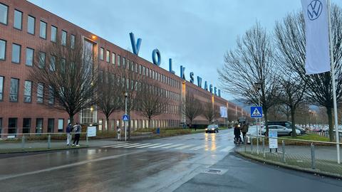 Blick auf das VW-Werk in Baunatal (Kassel). Auf dem Dach steht "Volkswagen" in großen Leuchtbuchstaben. Das Werk ist eine langgezogene Fabrikhalle mit vielen Fenstern.