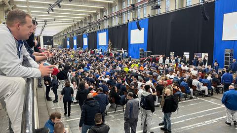 Blick in eine Halle des VW-Werks in Baunatal (Kassel). Auf einer Rampe stehen Beschäftigte und blicken nach unten in die Halle. Dort haben sich mehrere tausned Mitarbeiter kurz vor der Betriebsversammlung eingefunden.