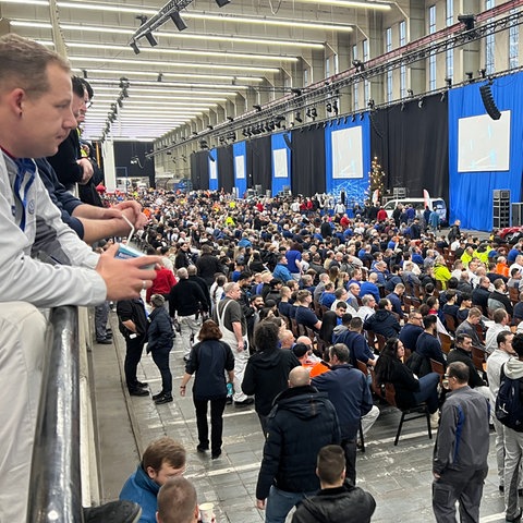 Blick in eine Halle des VW-Werks in Baunatal (Kassel). Auf einer Rampe stehen Beschäftigte und blicken nach unten in die Halle. Dort haben sich mehrere tausned Mitarbeiter kurz vor der Betriebsversammlung eingefunden.