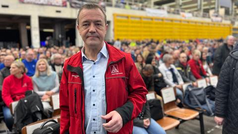 Betriebsratschef Carsten Büchling steht in einer Halle vor unzähligen Beschäftigten. Er trägt eine rote Jacke mit IG Metall-Logo und ein hellblaues Hemd.