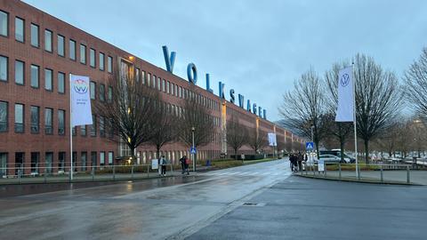 Blick auf das VW-werk in Baunatal (Kassel). Auf dem Dach steht "Volkswagen" in großen Leuchtbuchstaben. Das Werk ist eine langgezogene Fabrikhalle mit vielen Fenstern.