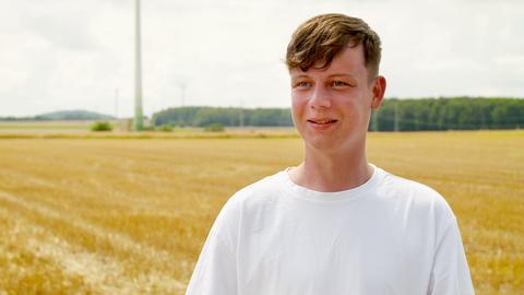 Portrait eines jungen Mannes, der in der Landschaft in einem Acker steht.