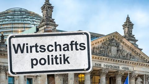 Ein weißes Hinweisschild mit der Aufschrift "Wirtschaftspolitik", befestigt mit Schrauben an einem Schilderpfahl, vor dem dem Berliner Reichstagsgebäude - es handelt sich u m eine Bildmontage